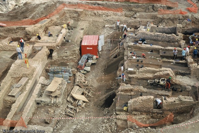 Vue de hauteur du chantier en cours de fouille. A droite de l'image, les archéologues s'affèrent sur les vestiges des ateliers-boutiques, à gauche, sur ceux de la voirie antique.