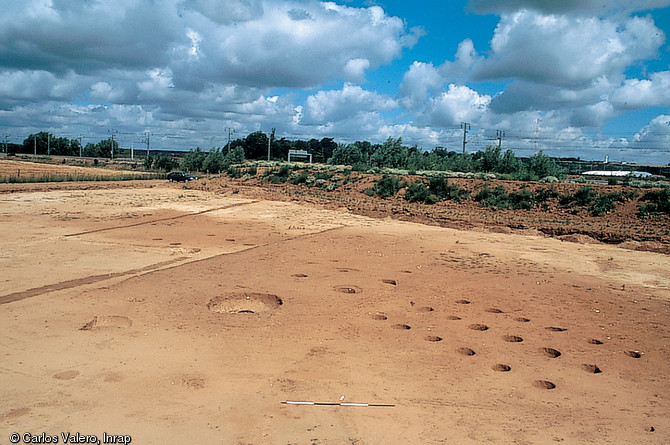 Vue de la fouille d'un bâtiment du premier âge du Fer à Marolles-sur-Seine (Seine-et-Marne), 1998.  Les creusements circulaires, traces laissées par d'anciens trous de poteaux en bois, trahissent l'emplacement d'éléments architecturaux aujourd'hui disparus, vestiges fugaces de bâtiments à ossature de bois. 