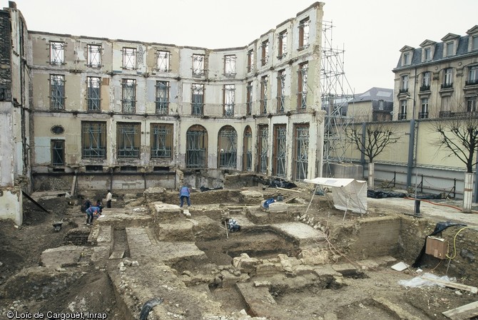 Fouille à l'emplacement de la future médiathèque de Reims (Marne), 2000.  Au pied de la façade conservée d'un ancien commissariat, on observe des solins (fondations légères) du haut Moyen Âge et des niveaux de sol du bas Moyen Âge. Au premier plan on trouve quelques blocs de fondation du rempart du IVe s. de notre ère.   