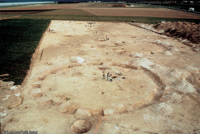 Photo aérienne d'une nécropole de l'âge du Bronze ancien, fouillée en 1989 sur le tracé du TGV nord (Pas-de-Calais).  Au premier plan se trouve un enclos funéraire mesurant 26 m diamètre qui comportait une sépulture à inhumation et une autre à incinération. 