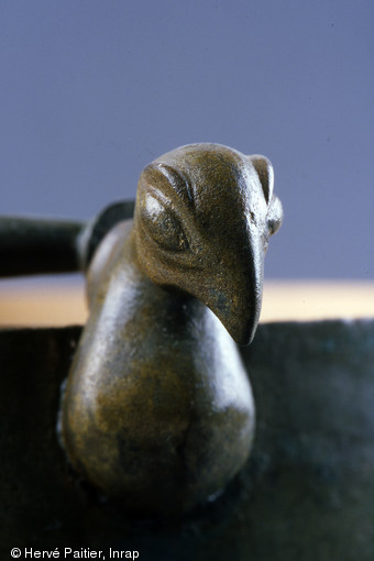 Tête d'oiseau en bronze vue de face mise au jour à Bucy-le-Long (Aisne). Elle ornait un rivet de fixation d'anse de seau. Deuxième âge du Fer (vers 120 avant notre ère).