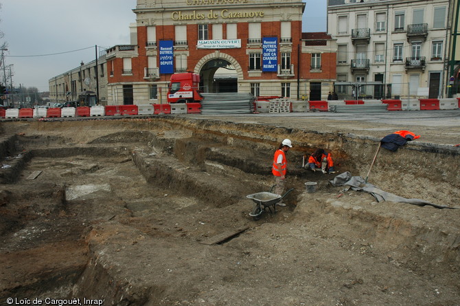 Fouille place de la République à Reims (Marne), 2007-2008.  Au premier plan les niveaux antiques, constitués de structures édifiées le long du cardo maximus (la voie principale nord-sud de la cité antique) révélé par la fouille. Au second plan, là où travaillent les deux archéologues, on observe une voie médiévale qui a traversé et perturbé les niveaux archéologiques plus anciens. 