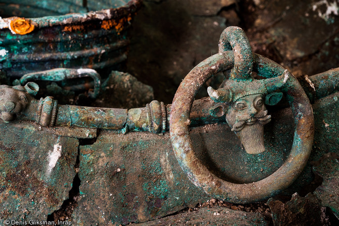 Vue de détail des anses d'un chaudron  au décor figurant le dieu-fleuve Acheloos, trouvé dans un complexe funéraire daté du Ve s. avant notre ère à Lavau (Aube) en 2015. À l'arrière plan une ciste (seau) en bronze. 