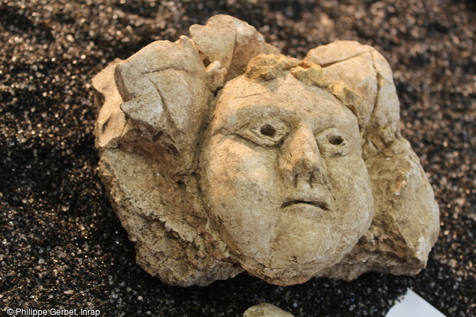 Détail d’un visage joufflu cerné de feuillages et retrouvé à Entrains-sur-Nohain (Bourgogne).