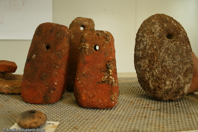 Ensemble de trois pesons en terre cuite, un poids en granite et au premier plan une petite fusaïole révélant la présence d’une activité de tissage sur le site gallo-romain de Bédée-Pleumeleuc (Bretagne), 2016.