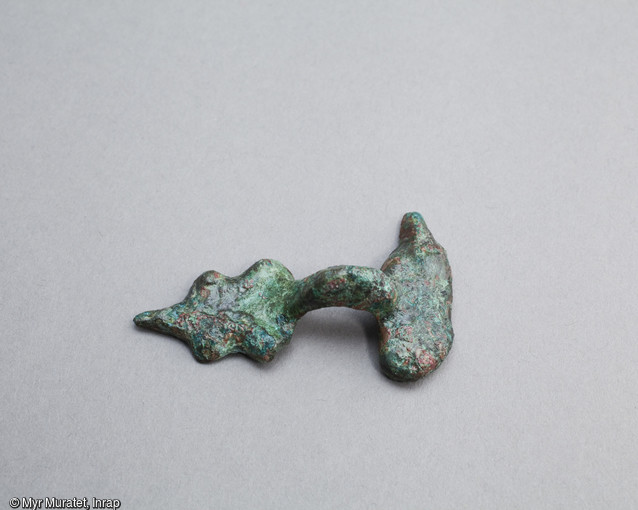 Anse de récipient en bronze, longueur 5,5 cm, 1er siècle avant notre ère, découvert sur le site archéologique de la place De Gaulle à Orléans (Loiret). Elle devait être accompagnée d'un anneau passé dans la boucle de l'anse. Le vase pouvait ainsi être mis en suspension.