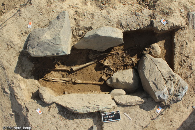 Tombe à inhumation entourée de dalles, de la fin de l'âge du Bronze  mise au jour à Massongy (Haute-Savoie). Le squelette est celui d'une femme qui portait autour du cou un collier d'ambre. La stèle gravée de signalisation de la sépulture s'est effondrée sur le squelette.  