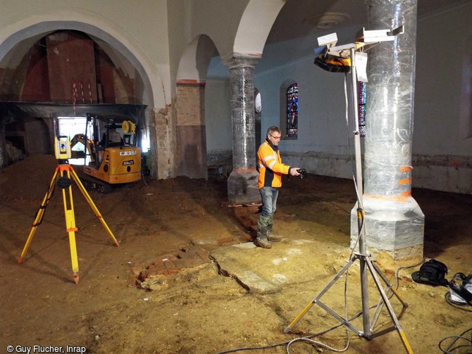 Décapage à la mini pelle électrique et test d'orthophotographie dans l'église Sainte-Benoite de Lerzy (Aisne). On distingue au sol la fondation de l'arc triomphal d'époque romane et un lambeau de sol en brique d'époque moderne.