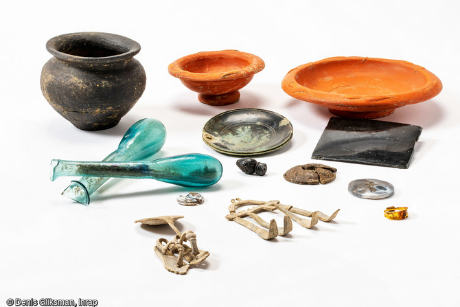    Une partie du mobilier issu de la fouille du riche dépôt découvert à Alba-la-Romaine (Ardèche), 2021.  Il est composé de vases en céramiques, de balsamaires en verre, de deux miroirs, d'une bague en or, de deux miniatures en plomb, d'un jeton en os brulé et d'éléments en os brûlé d’un volumen.     
