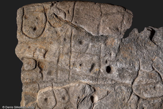 Vue de détail du quart supérieur gauche de la dalle de Saint-Bélec découverte à Leuhan (Finistère). On observe sur ce clichés des motifs dégagés en bas-relief, des formes ovalaires et des cupules piquetées et un motif en échelle pour partie incisé.
