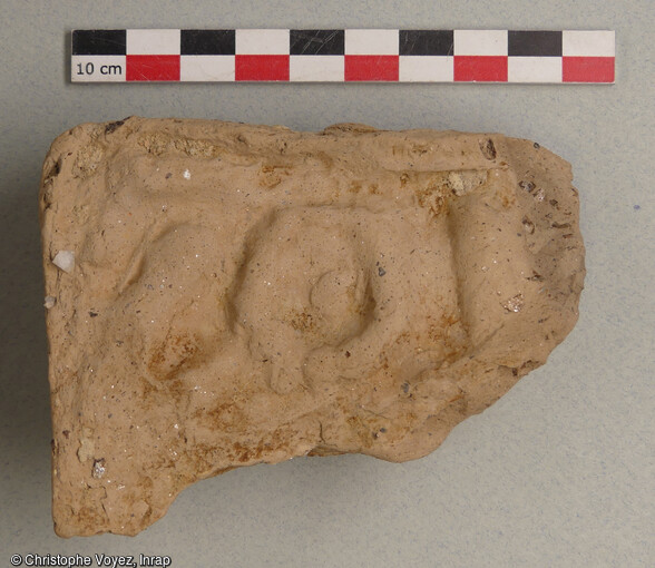 Fragment d'antéfixe (ornement de toiture) en terre cuite de fabrication massaliète (IVe siècle av. notre ère). Il porte un décor moulé non identifiable. Découvert dans une fosse mise au jour à Marseille (Bouches-du-Rhône) en 2021, qui était utilisée pour rejeter des résidus d'un atelier de potiers qui devait se situer à proximité. 