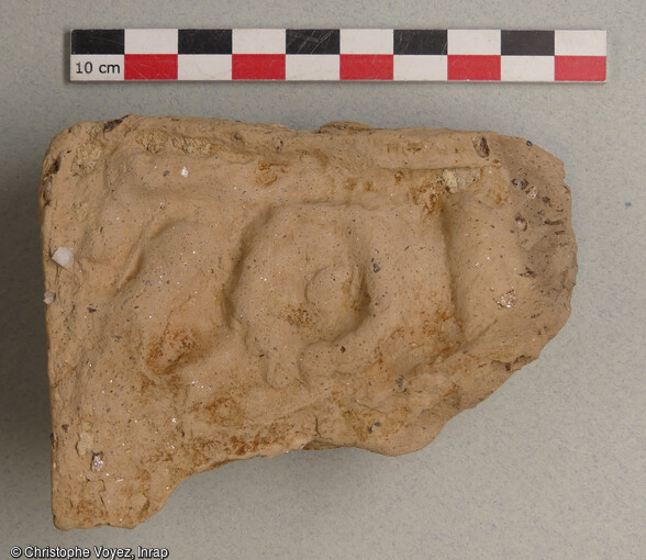 Fragment d'antéfixe (ornement de toiture) en terre cuite de fabrication massaliète (IVe siècle av. notre ère). Il porte un décor moulé non identifiable. Découvert dans une fosse mise au jour à Marseille (Bouches-du-Rhône) en 2021, qui était utilisée pour rejeter des résidus d'un atelier de potiers qui devait se situer à proximité.