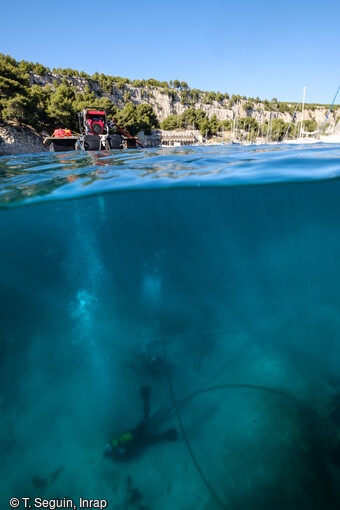 Un plongeur-archéologue réalise un sondage dans la calanque de Port Miou (Cassis), grâce à un aspirateur à sédiment alimenté par une motopompe sur un ponton en surface.