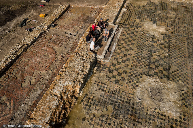 Vue aérienne des pavages de la galerie-couloir et de la salle d'apparat de la résidence aristocratique des évêques de Thérouanne à Saint-Martin d'Hardinghem (Pas-de-Calais) datant du second Moyen Âge. Ces pavages couvrent une surface totale de 200 m2 bien conservés. Les carreaux présentent des motifs variés, caractéristiques de cette période : lions, aigles, poissons, fleurs de lys, marguerites, chevaliers, figures héraldiques. Majoritairement carrés de 10x10 cm, ils sont disposés en panneaux séparés par des bandes monochromes.