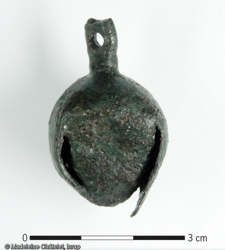 Grelot médiéval en alliage cuivreux. Il est composé de quatre lobes repliés vers l'intérieur. Une languette est percée au sommet pour la suspension. Il provient d'un bras fossile d'un cours d'eau (paléochenal) situé sur le site.  Long. 3.4 cm ; Larg. 2.1 cm ; poids. 12.9 gr   