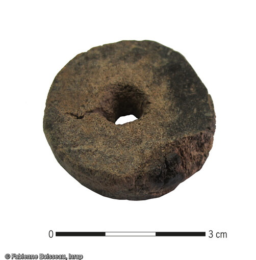 Portion cylindrique de merrain utilisé pour réaliser une fusaïole : la surface perlée a été grossièrement raclée et une perforation circulaire a été aménagée dans le corps spongieux. Dimensions : Diam. : 4,1 cm ; ép. 1,2 cm. Il est issu d'une cabane dont le mobilier céramique n’a pas permis d’attribution plus précise que le Moyen Âge indéterminé.