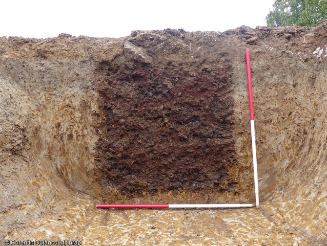 Vue en coupe de la fondation d'un des bâtiments remplie de scories de réduction de fer mis au jour au cours de la fouille du site antique à Saint-Valérien (Yonne). L'emploi de ce matériau présent dans les fondations en tranchée étroite, pouvait avoir une fonction drainante dans un terrain soumis à de fréquentes remontées de la nappe phréatique. Ces scories témoignent aussi de l'intensité de la production du fer à l'époque romaine dans cette région riche en minerai. 