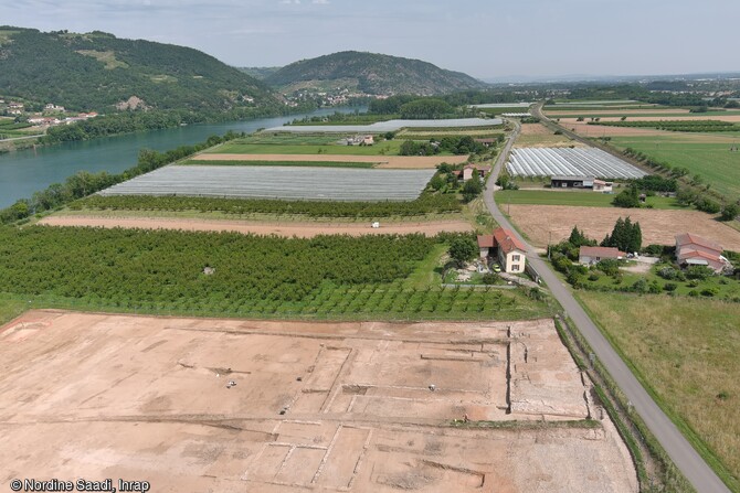 Vue aérienne de la fouille sur la rive gauche du Rhône à Laveyron (Drôme). En élévation sur la rive droite le monument antique de La Sarrasinière. La fouille en cours, met au jour un établissement dédié à la vinification, construit au 1er s. de notre ère. Cet établissement, situé sur le territoire des Allobroges (peuple gaulois dont le territoire s'étendait entre l'Isère, le Rhône et les Alpes du nord), produisaient probablement un vin très prisé des Romains et mentionné dans les textes anciens (le vinum picatum). 