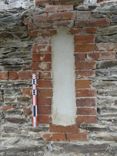 Baie en brique, antérieure aux enduits peints - mur gouttereau nord - extérieur. La première phase de construction de l'église du XIVe siècle de l'ancienne chartreuse de Sainte-Croix-en-Jaretz (Loire) correspond à l'édification d'une vaste nef quadrangulaire éclairée depuis le nord par plusieurs fenêtres construites en briques.