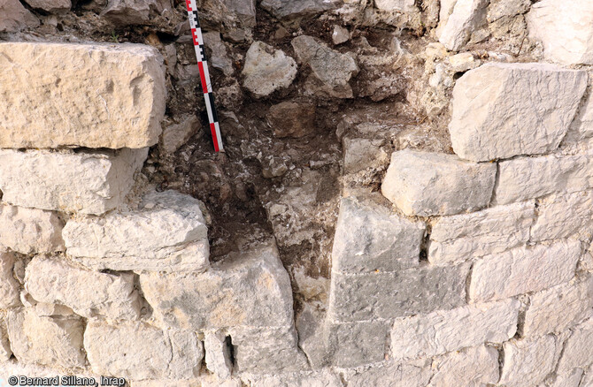 Détail de l'archère 76 de la tour sud du château Saint-Marcel à Marseille (Bouches-du-Rhône). Il s'agit d'une archère en capitale (c'est-à-dire bissectrice) à ébrasement simple équipée d'une plongée qui permet un tir plongeant. L'extrémité inférieure de la fente n'est pas évasée en étrier. Ce sont des marqueurs qui permettent d'attribuer la tour aux fortifications capétiennes précoces, en l'occurrence à Charles 1er d'Anjou, frère de Louis IX, qui occupe le château entre 1264 et 1276. 