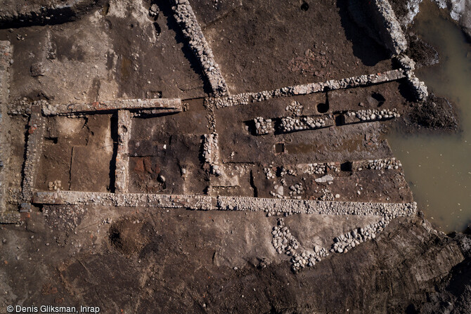 Vue aérienne du mithræum et de ses annexes, érigé autour de l'an 100 de notre ère sur le site de l'antique colonie romaine de Mariana à Lucciana (Haute-Corse). Ce sanctuaire se compose de plusieurs espaces dont une salle de culte et son antichambre. La salle d'assemblée, rectangulaire (11x5m), est constituée d'un couloir central, bordé de deux longues banquettes de 1,80 m de largeur. En vis-à-vis, deux niches voûtées en briques sont aménagées dans les banquettes. A l'extrémité du couloir devait se dresser le bas-relief représentant Mythra. 