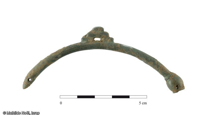 Fragment de torque de type ternaire en alliage cuivreux. Une extrémité est en pointe perforée, l'autre comprend un bulbe creux et percé d'une moulure. Un appendice constitué de baguettes orne la partie supérieure. Ce type de bijou est connu pour le début de la période gauloise (fin du IIIe siècle avant J.-C.). Il s'agirait d'un objet ancien hérité sur plusieurs génération découvert sur l'occupation de la fin de la période gauloise mise au jour à Meung-sur-Loire (Loiret: Les Bouillants et la Maison Neuve ).Diamètre de 15 cm.
