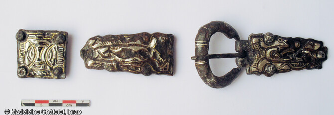 Cette garniture de ceinture tripartite (fermoir, contre-ferrure et ferrure dorsale) a été découvert dans une tombe d'homme. Elle est composée d’une plaque-boucle et d’une contre-plaque de forme trapézoïdale fixées à la ceinture par trois rivets en fer plaqués d’argent. La plaque dorsale, carrée, est dotée aux quatre angles de rivets en fer. Elle est datée du 2e tiers du VIIe siècle.