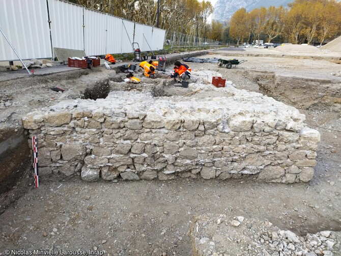 Vue du mur méridional de l'édifice. Parmi les vestiges mis au jour figure, en limite d’emprise, un édifice quadrangulaire, arasé au niveau des premiers sols de l’Esplanade. La fouille a montré qu’il avait été fondé sur une légère surélévation de la terrasse alluviale, qu’il a été construit d’un seul tenant, sans reprises manifestes, et que son côté oriental était protégé par un fossé drainant. Grâce aux datations effectuées lors du diagnostic, cet édifice était au moins utilisé au début de la Période Moderne – ce qui en fait la première occupation connue de l’emprise fouil