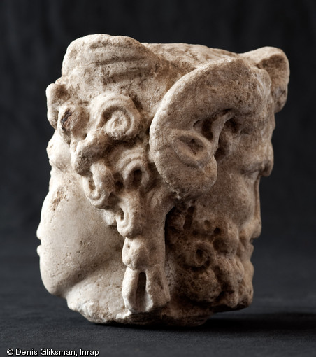 Tête en marbre à deux visages adossés formant le sommet d'un pilier hermaïque : un visage juvénile opposé à un visage de personnage plus âgé (vue de profil). Fouille du Faubourg d'Arroux, Autun (Saône-et-Loire), 2010.