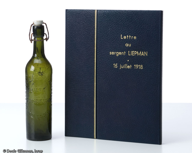 Lettre au sergent Liepman datée de 1918 après restauration et la bouteille de Champigneulles dans laquelle elle a été découverte. Fouille d'un site mérovingien à Messein (Meurthe-et-Moselle), 2004.  Elle est datée d'Oklahoma City le 15 juillet 1918. Ce courrier est adressé au sergent Morres Vickers Liepman, étudiant à Pittsburg (Kansas) engagé dans l'armée américaine le 25 juillet 1917. Arrivé au Havre en juin 1918, il participe aux batailles d'Argonne, de Saint-Mihiel, de Verdun et des Vosges.