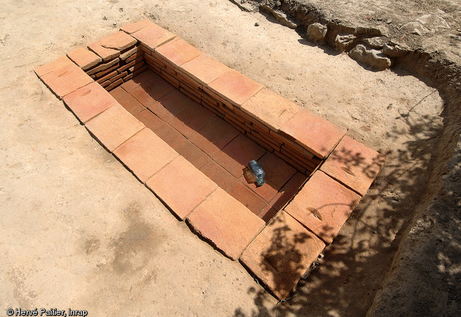 Sépulture à inhumation d’un enfant (8 - 9 ans) dans un caveau en briques (longueur 2,40 m, largeur 1 m), IIe-IIIe s. de notre ère, Neuville-sur-Sarthe (Sarthe), 2010.  La mise au jour d’une telle tombe dans l’enceinte sacrée d’un temple gallo-romain pose la question de leur éventuelle contemporanéité, en effet il est de règle à l’époque gallo-romaine de séparer ce qui est « pur » (les temples) de ce qui est « impur » (les inhumations par exemple).