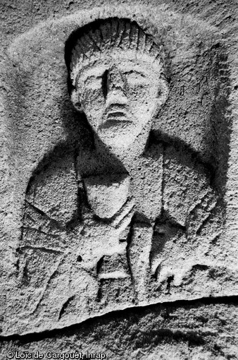 Stèle funéraire gallo-romaine en arkose (hauteur 74 cm, largeur 43 cm), nécropole de Pont-L'Évêque, Autun (Saône-et-Loire), 2004.  La tête de ce personnage en buste a été sculptée avec soin, lui donnant une expression sévère. Sa main droite tient un grand gobelet à pied, tandis que la main gauche est fermée sur le manche d'un marteau : ce dernier attribut laisse penser que le défunt était un sculpteur de pierre ou un artisan du fer. 