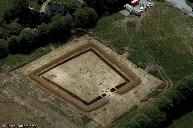 Vue aérienne en fin de fouille de l'habitat gaulois de Corps-Nuds (Ille-et-Vilaine), daté entre la fin de La Tène moyenne et la fin de La Tène finale, 2009. Un fossé trapézoïdal délimite un espace occupé par neuf bâtiments sur poteaux (habitat et annexes agricoles). L'unique accès à l'espace interne s'effectue par un porche monumental.
