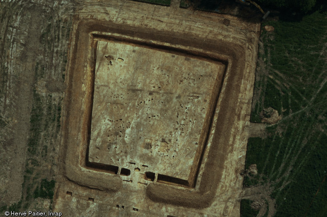 Vue aérienne de la ferme gauloise de Corps-Nuds (Ille-et-Vilaine), datée entre la fin de La Tène moyenne et la fin de La Tène finale, 2009.  Au centre de l'enclos trapézoïdal se développent les différents bâtiments, tandis qu'au premier plan on remarque les vestiges du porche monumental marquant l'entrée de la ferme.  