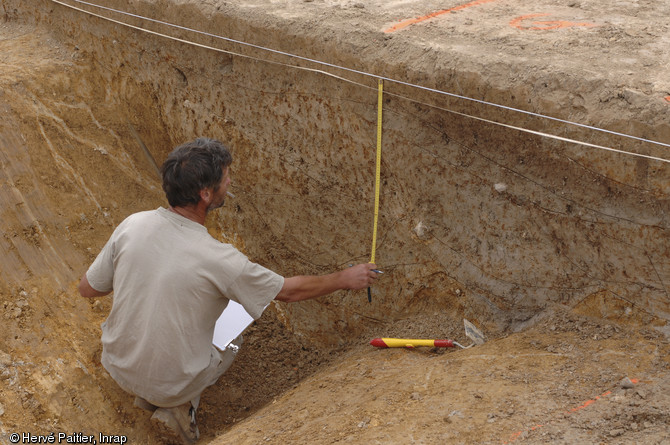 Un archéologue relève une coupe stratigraphique du fossé de l'enceinte.