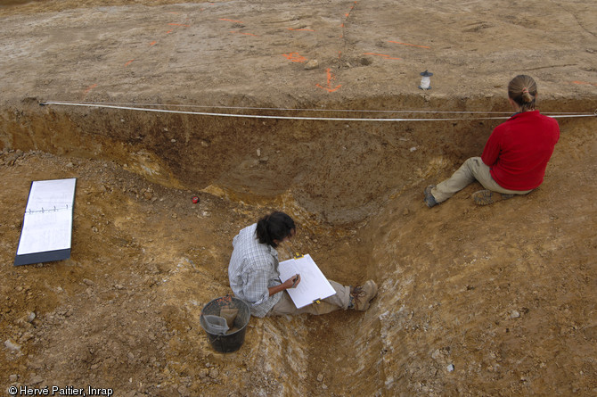 Deux archéologues relèvent une coupe stratigraphique du fossé de l'enceinte.