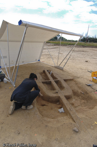 Une archéologue dégage une sépulture en coffre de bois située au centre de l'un des tumulus du site.