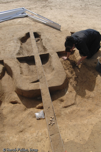 Une archéologue dégage une sépulture en coffre de bois située au centre de l'un des tumulus du site.