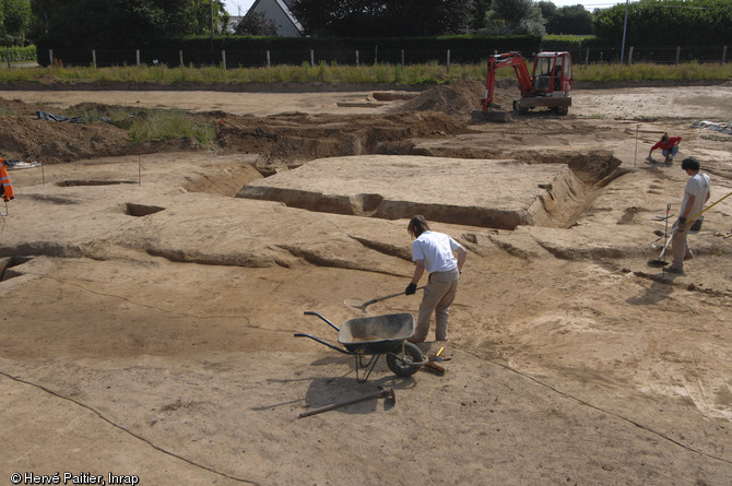 Les archéologues nettoient un enclos quadrangulaire avant la photographie.
