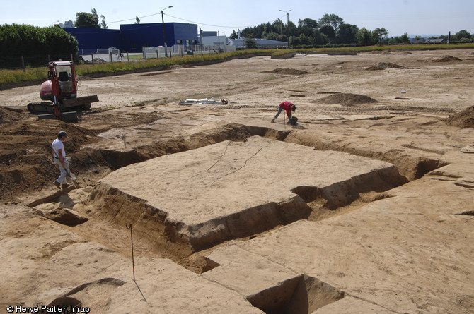 Les archéologues nettoient un enclos quadrangulaire avant la photographie.