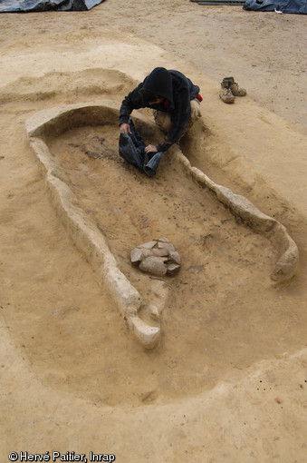 Une archéologue dégage une sépulture en coffre de bois située au centre de l'un des tumulus du site.