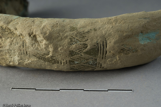 Détail d'un décor conservé sur un des sept bracelets en bronze découverts dans un vase en terre cuite à l'occasion d'un diagnostic mené à Domloup (Ille-et-Vilaine) en 2009. Par leurs caractéristiques, ils peuvent être datés des environs de 1300 avant notre ère.  