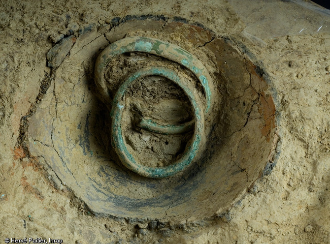 Les deux derniers bracelets de bronze du dépôt de Domloup (Ille-et-Vilaine) encore en place, 2009.  Cette découverte est particulièrement intéressante car les publications sur les rares dépôts de bracelets comparables à celui de Domloup sont anciennes et nous renseignent peu sur le contexte de découverte. 