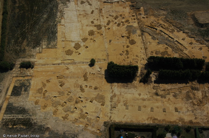 Vue aérienne de l'établissement rural de Brem-sur-Mer (Vendée), 2006. Les ouvertures pratiquées dans le sol visibles sur la photo correspondent aux différents sondages pratiqués sur le tracé du fossé.  Ce système d'enclos renfermant des bâtiments sur poteaux pourrait correspondre à un lieu de gestion du bétail. 