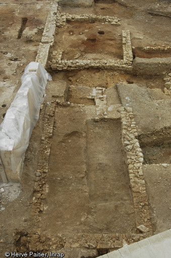 Vue des trois états successifs de la forge mise au jour dans l'enceinte du château de Caen (Clavados), 2005.  Au premier plan la forge de la seconde moitié du XVe s., à l'arrière-plan on distingue la forge du XIIIe s., et à gauche, couvert d'une bâche, le mur gouttereau de la forge des XIVe et XVIe siècles. L’agrandissement important du bâtiment au XIVe s. a été mis en relation avec la Guerre de Cent Ans. 