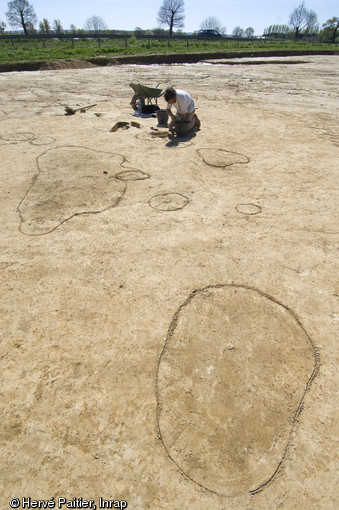 Dégagement d'une fosse de l'âge du Bronze à Bédée (Ille-et-Vilaine), 2011.  Les formes plus sombres délimitées au sol correspondent à des structures archéologiques en creux comme des fosses ou des trous de poteaux. 