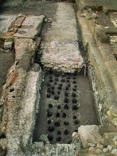 Fondations d'un mur en milieu humide, IIIe s. de notre ère, site du Vieux-Port à Reims (Marne), 2007-2009.  Des pieux en chêne sont enfoncés dans la vase à intervalles réguliers et recouverts par un radier constitué d'un mélange de pierres et de craie compactée. La largeur des fondations atteint 1,50m.  Photo publiée dans le numéro 23 de la revue de l'Inrap Archéo