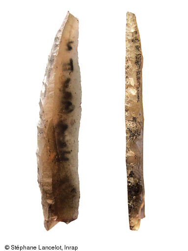 Armature microlithique (L=3,15cm) provenant du site de Hangest-II nord (Somme), Mésolithique, 1989.  Ce segment porte des traces (en noir) de colle d'emmanchement.   Photo publiée dans le numéro 28 de la revue de l'Inrap Archéopages.