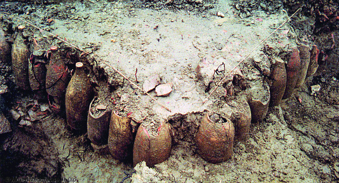 Un des alignements d'amphores mis au jour lors des fouilles menées sur l'Île des Sables à Arles (Bouches-du-Rhône) en 1990.  La disposition de cet aménagement (en angle droit, amphores pointe en haut) laisse penser qu'il revêt une fonction de drain ou de vide sanitaire.  Photo publiée dans le numéro 29 de la revue de l'Inrap <a class= rte-link-ext  href= http://www.inrap.fr/archeologie-preventive/Recherche-scientifique/Archeopages/Les-numeros/28-29-30-HS02-2010/Numero-29/Dossier-Recyclage-et-remploi/p-11771-De-vita-amphorarum.-La-revalorisation-des-amphores-en-contextes-humides.