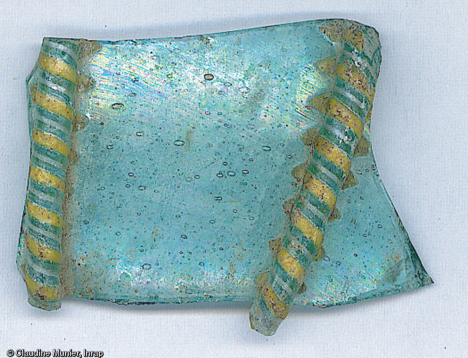 Fragment d'un bol en verre de teinte translucide bleue-verte daté du IXe s., décoré de baguettes rapportées ornées de fils opaques jaunes et blancs, provenant des fouilles du 12 rue Saint-Genest à Nevers (Nièvre) menées en 2004. 